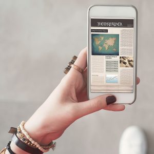 Woman holding coffee reading newspaper on smartphone