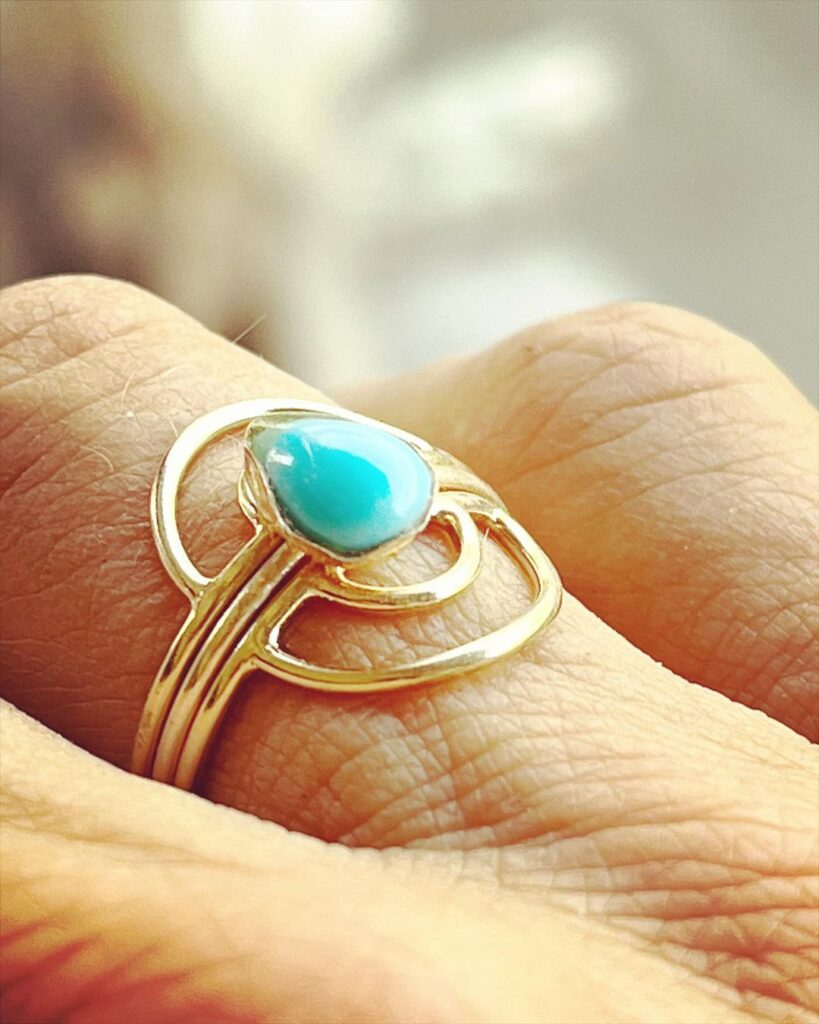 A gold ring with a small turquoise stone on a finger