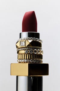 A lipstick tube with assorted gold rings with lab-grown diamonds stacked on it.