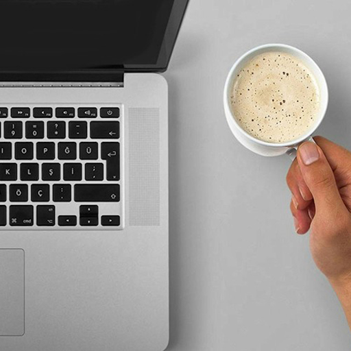 Laptop next to a hand holding a coffee mug.