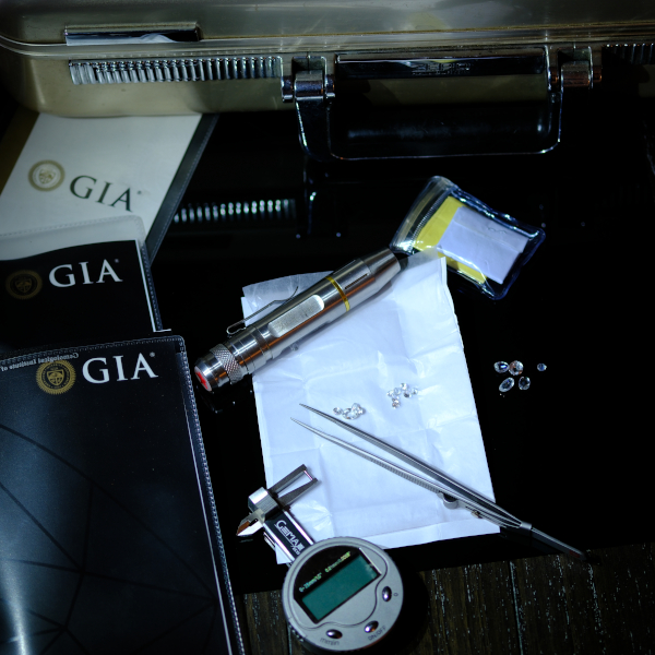 A parcel of diamonds is laid out beside a series of GIA lab certificates and a briefcase